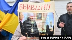 Жена държи снимка, на която митрополит Павло - игумен на манастира, стои до руския президент Владимир Путин, с надпис "Убийци!!!", докато хора се събират на входа, 28 март 2023 г.