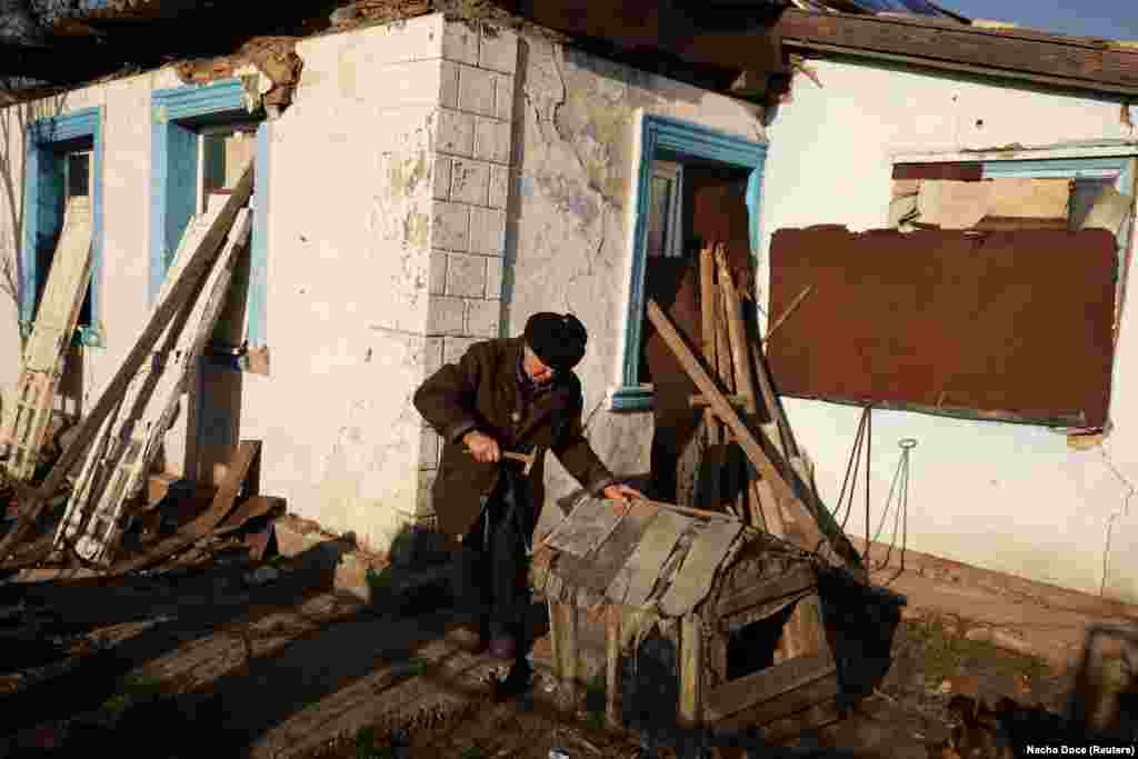 Volodymyr repairs a doghouse in front of his shattered home where boards cover the blown-out windows.