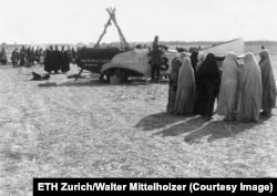 Burkába öltözött nők nézik, ahogy Walter Mittelholzer repülőgépét javítják egy Teherántól negyven kilométerre fekvő településnél 1924 decemberében