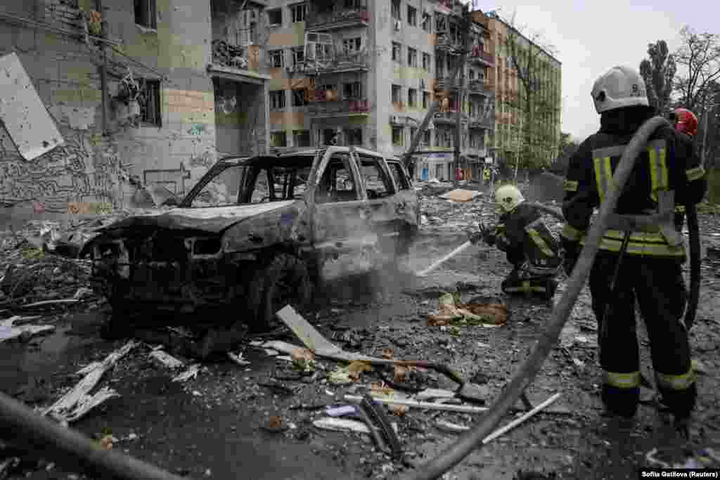 Firefighters extinguish a fire that destroyed a car near the residential buildings.