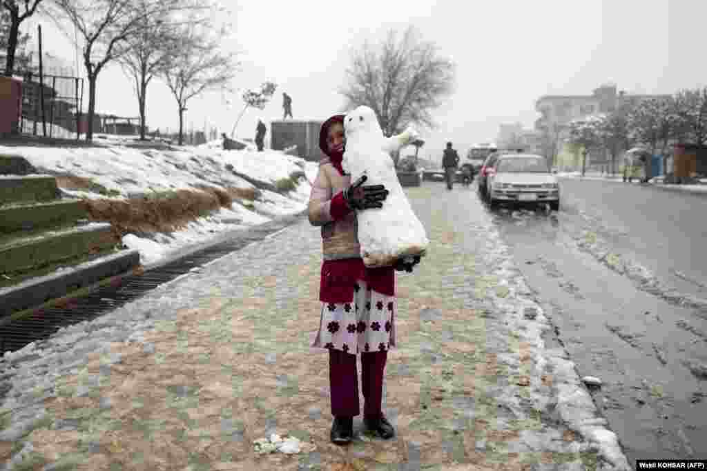 An Afghan girl carries a snowman along a sidewalk in Kabul.&nbsp;