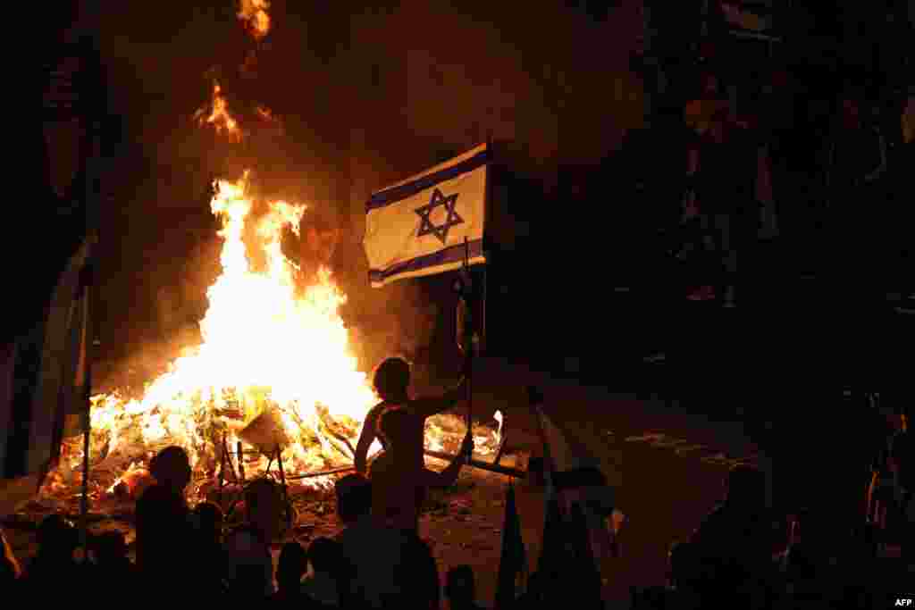 Protestuesit me flamuj kombëtarë në duar të mbledhur rreth një zjarri në Tel Aviv.