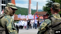 Punonjësit serbë të një spitali gjatë një marshimi protestues në komunën e Zveçanit, në veri të Kosovës, ndërsa paqeruajtësit kujdesen për ruajtjen e sigurisë, 19 qershor 2023.