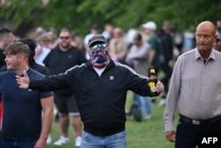  Маскиран протестиращ прави жест към служители на реда по време на демонстрацията 