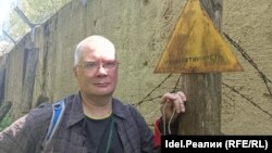 Андрей Ожаровский у выцветшего знака "Радиоактивность". За его спиной бетонный забор хранилища.