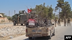 SYRIA - Syrians sit in the back of a passing pick-up truck as Turkish soldiers deploy at the site of an improvised explosive device which hit a joint Turkish-Russian patrol in Idlib, July 14, 2020.