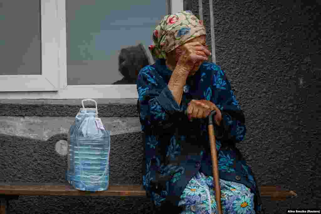 Further along the Dnieper River, Hanna, an elderly resident of the village of Hrushivka, sits next to bottles of water that she received as aid.