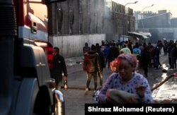 Луѓето поминуваат покрај зграда по смртоносниот пожар во раните утрински часови, во Јоханесбург, Јужна Африка