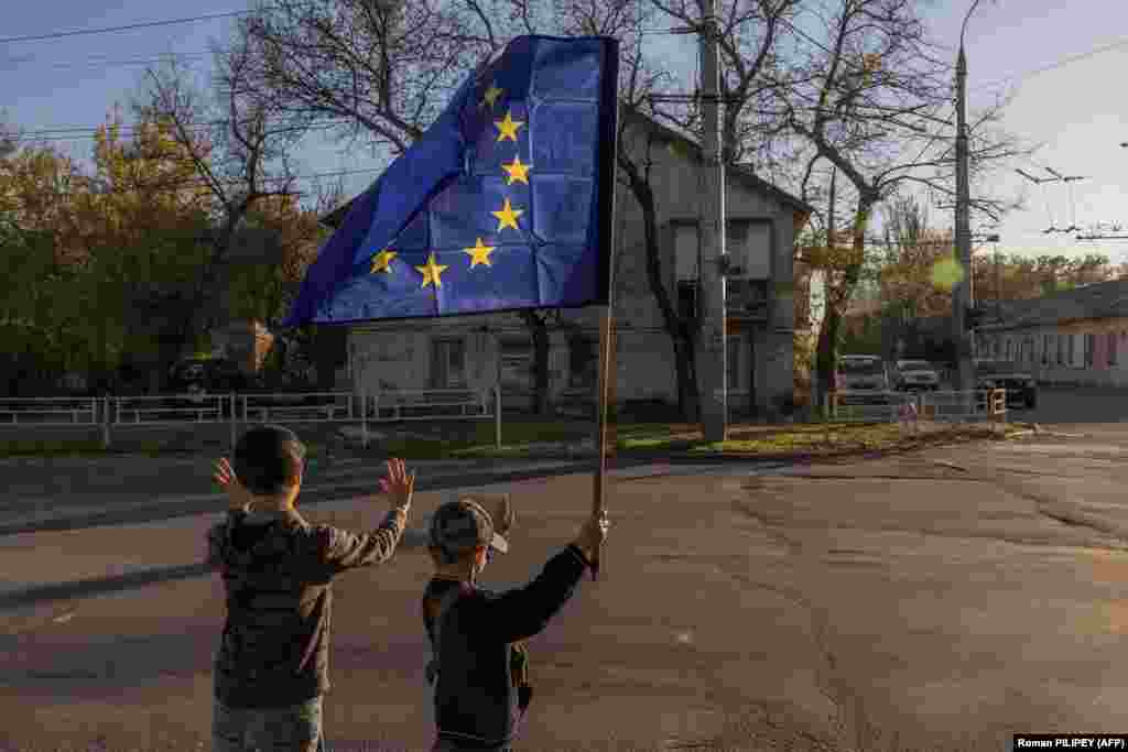 Children wave a European Union flag at passing cars in the southern Ukrainian city of Kherson on October 29. Residents in the beleaguered regional capital are going on with their lives despite the risks of indiscriminate shelling from Moscow&#39;s forces, which can maim and kill at any time.
