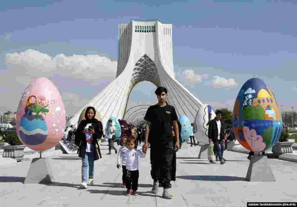 A family walks between colorful decorations in the shape of eggs, a symbol of Norouz, or the Persian New Year, in Tehran&#39;s Freedom Square.&nbsp;