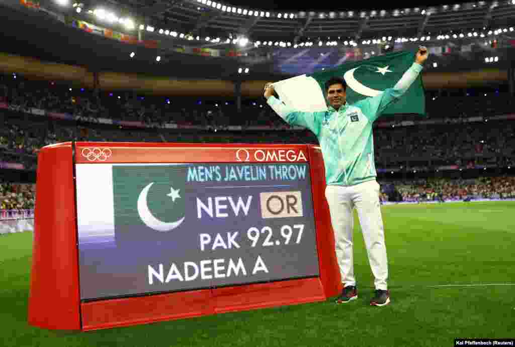 Arshad Nadeem of Pakistan celebrates with his national flag after winning gold in the men&#39;s javelin competition as he stands next to a screen displaying his new Olympic record on August 8.