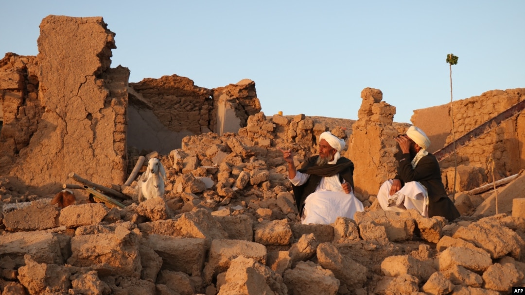 Afghan men sit beside a damaged house after an earthquake in Afghanistan's Herat Province on October 7.