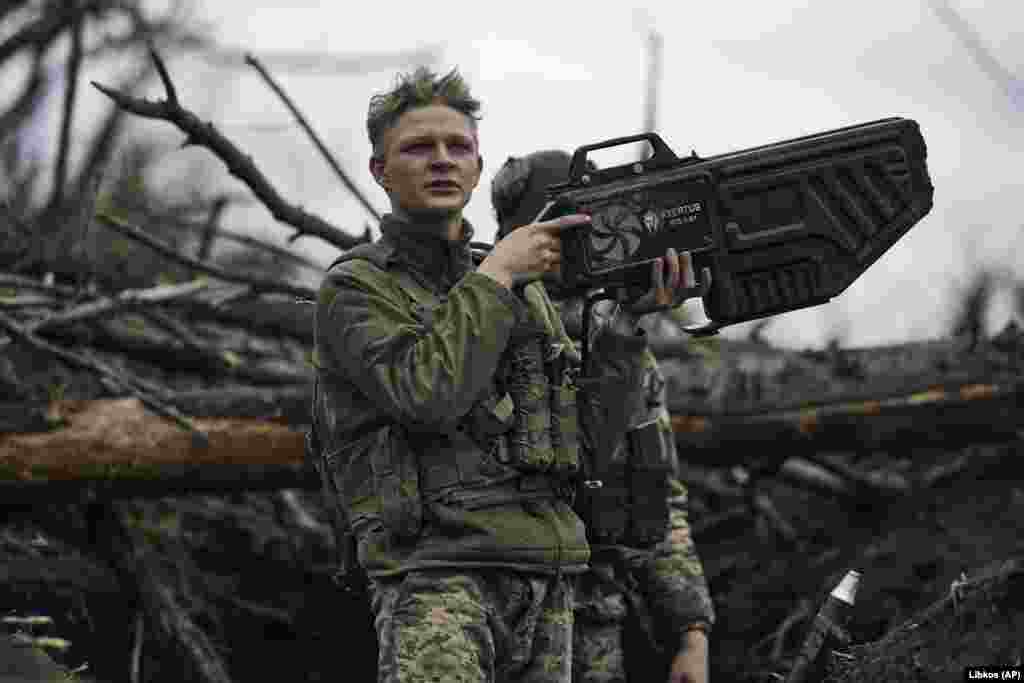 Një ushtar ukrainas mban një armë antidron në një pozicion në vijën e parë të frontit pranë Avdivkas në prill të vitit 2023. Pajisja prej 11.300 dollarësh e prodhuar në Ukrainë që shihet në këtë imazh, përdor valët e radios për të mposhtur lidhjen midis një droni dhe operatorit të tij. Ndërhyrja mund të ndërpresë furnizimin me video të dronit dhe, në varësi të modelit të dronit, mund ta detyrojë atë të kthehet në pikën e tij të ngritjes, të ulet menjëherë ose të largohet me erën dhe përfundimisht të rrëzohet.