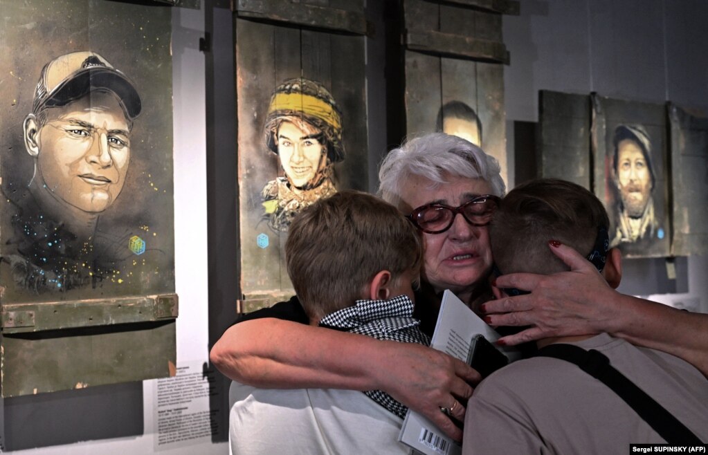 Parenti di soldati ucraini deceduti davanti ai ritratti dipinti dallo street artist francese Christian Guemy.  La sua mostra Guerre En Ukraine (Guerra in Ucraina) è stata inaugurata l'8 luglio presso il Centro espositivo del Museo della guerra di Kiev.