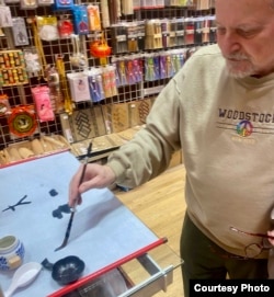 В магазине Чайнатауна. А. Генис выводит иероглифы на бумаге. Виден Рен, то есть Человек. Фото Ирины Генис, 2024