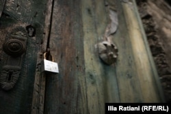 A padlock hinders visitors from entering this intricately carved house that is slowly rotting away.