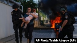 Сотрудники полиции эвакуируют женщину и ребенка с места попадания ракеты, выпущенной из сектора Газа, в Ашкелоне, на юге Израиля, в субботу, 7 октября 2023 года