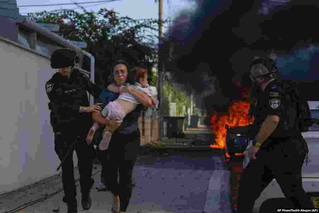 Полиция помогает эвакуироваться женщине с малышом с места ракетного удара в Ашкелоне, Израиль, 7 октября 2023 года.