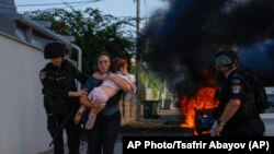 Полиция помогает эвакуироваться женщине с малышом с места ракетного удара в Ашкелоне, Израиль, 7 октября 2023 года
