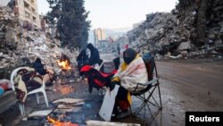 Luni, 13 februarie, oameni se încălzesc lângă un foc improvizat în Kahramanmaras, Turcia.