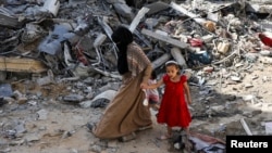 Një grua dhe një vajzë e vogël duke ecur nëpër rrënoja, pas sulmeve ajrore izraelite në kampin e refugjatëve Nuseirat në Rripin e Gazës më 9 qershor 2024. 