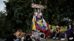 Бежанци седят под знак, обозначаващ границата между Панама и Колумбия, по време на пътуването си през прохода Дариен, 9 май 2023 г.