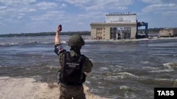 Представитель оккупационных войск России на левом берегу Днепра стоит напротив уничтоженной Каховской ГЭС, Украина, июнь 2023 года
