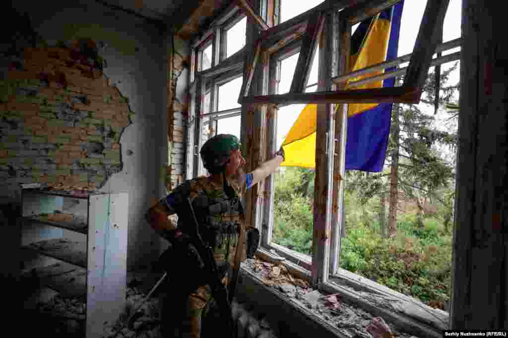 Un soldat ucrainean așează drapelul național, agățat pe Casa de Cultură din satul Blahodatne, 17 iunie 2023. Satul din regiunea Donețk a fost printre primele localități recucerite în contraofensiva ucraineană.