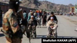 A Taliban security guard watches as young Afghan boys help elderly men in wheelchairs after gunfire between Afghanistan and Pakistan border forces near the Torkham crossing on February 20.