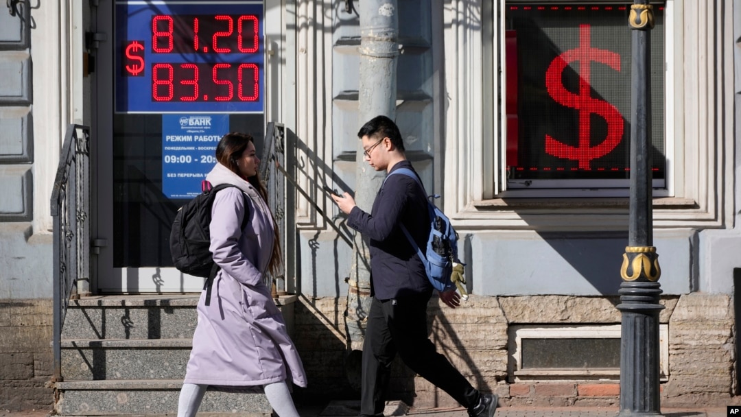 People walk past an exchange office screen showing the exchange rates of the U.S. dollar to the Russian ruble in St. Petersburg, Russia, in April 2023.