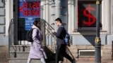 People walk past an exchange office screen showing the currency exchange rates of the U.S. dollar to the Russian ruble in St. Petersburg, Russia, in April 2023.