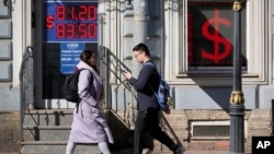 People walk past an exchange office screen showing the exchange rates of the U.S. dollar to the Russian ruble in St. Petersburg, Russia, in April 2023.