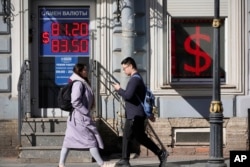 People walk past an exchange office screen showing the currency exchange rates of U.S. Dollar to Russian Rubles in St. Petersburg, Russia, on April 7.