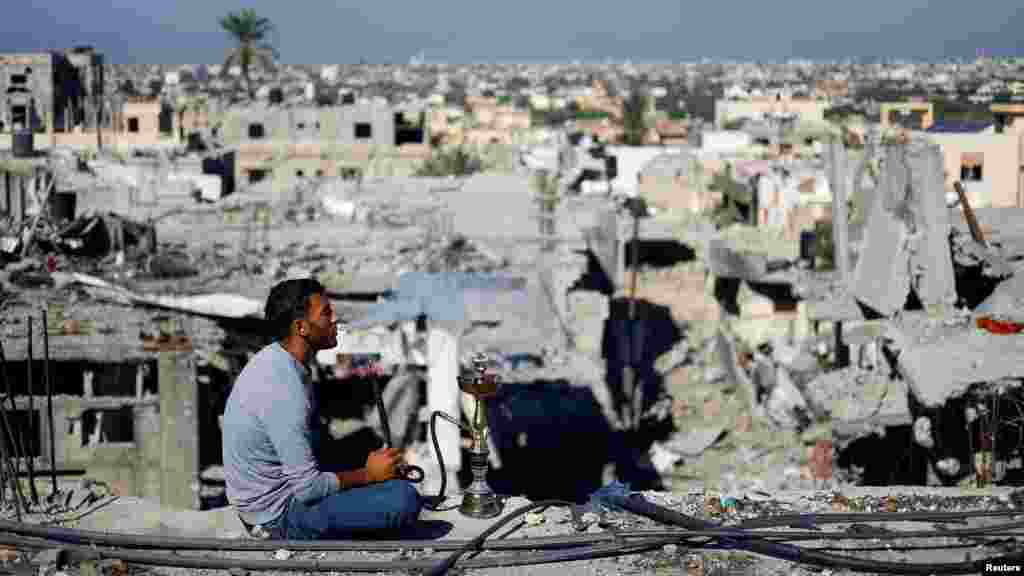 Egy palesztin férfi sisát szív, a háttérben a földdel egyenlővé tett Hán Júnisz 2023. november 29-én.&nbsp;A kárbecslést az ENSZ Műholdközpontja készítette, ahol az elemzők nagyon nagy felbontású műholdfelvételeket vizsgálnak, hogy megtalálják a sérült épületeket