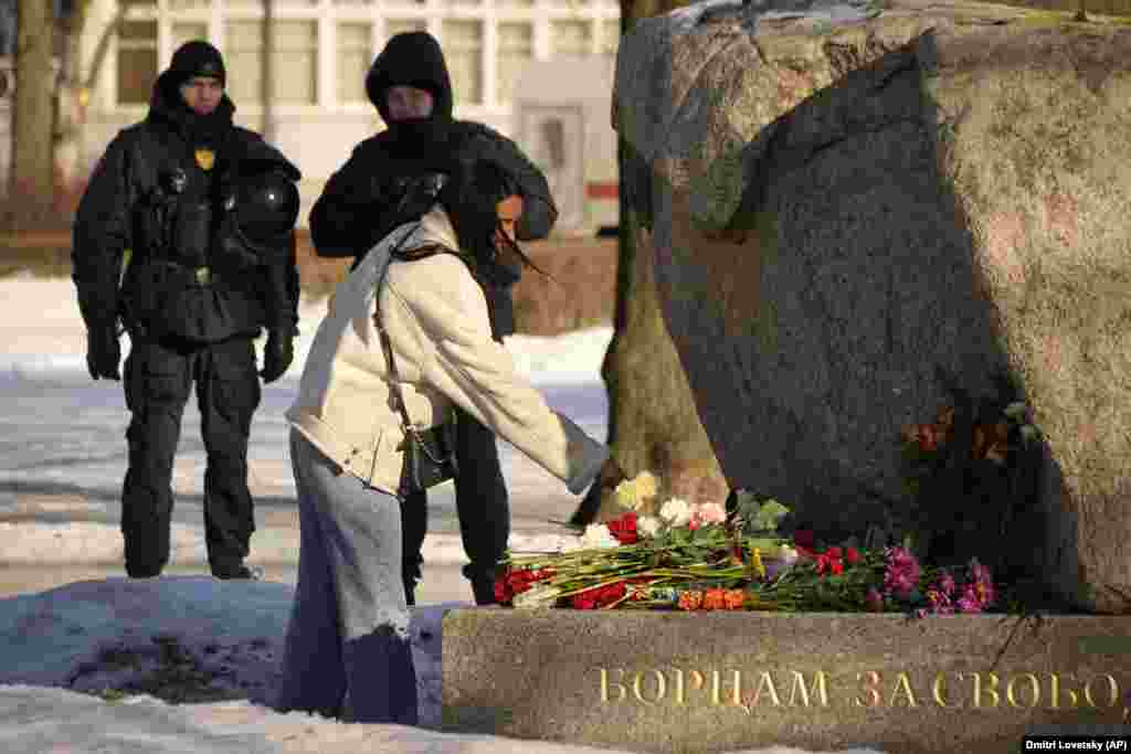 Police officers watch a woman laying flowers to pay tribute to Russian opposition leader Aleksei Navalny at a monument in St. Petersburg. Russians across the country streamed to ad hoc memorials with flowers and candles to pay tribute to Navalny, the Kremlin&#39;s fiercest critic. Navalny, 47, died in prison on February 16 under unclear circumstances. Hundreds have been arrested for paying tribute to his legacy.