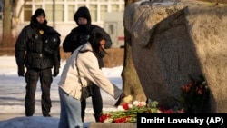 Police officers watch a woman laying flowers to pay tribute to Aleksei Navalny at a monument in St. Petersburg on February 18.