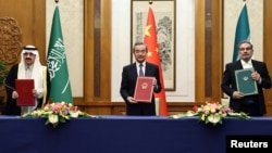 Top Chinese diplomat Wang Yi holds up a March 10 deal in Beijing with Secretary of Iran's Supreme National Security Council Ali Shamkhani and Saudi State Minister Musaad bin Muhammad al-Aiban.