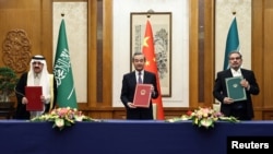 Najviši kineski diplomata Vang Ji drži sporazum potpisan 10. marta u Pekingu sa sekretarom iranskog Vrhovnog vijeća za nacionalnu sigurnost Alijem Šamhanijem i saudijskim državnim ministrom Musaadom bin Muhamedom al-Aibanom.