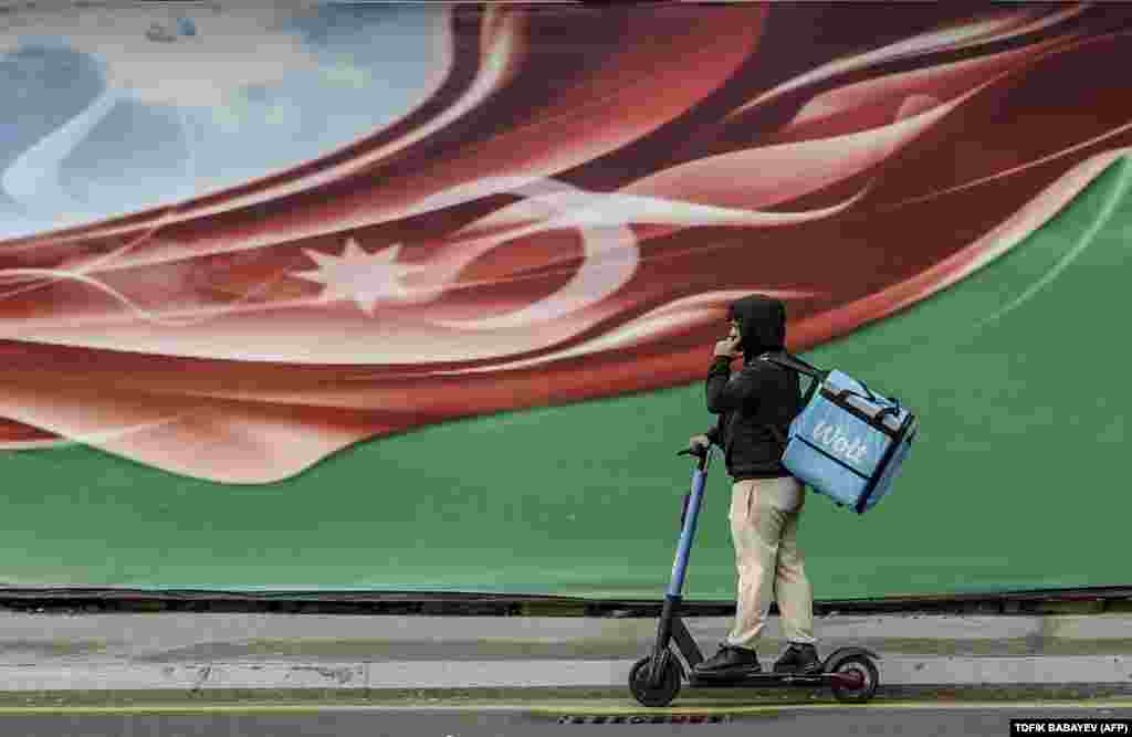 A courier rides past a poster in Baku.