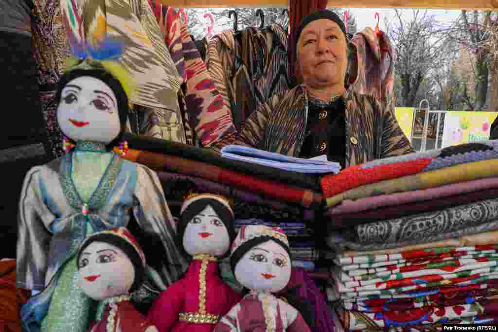Женщина торгует куклами и тканями на праздничной ярмарке&nbsp;