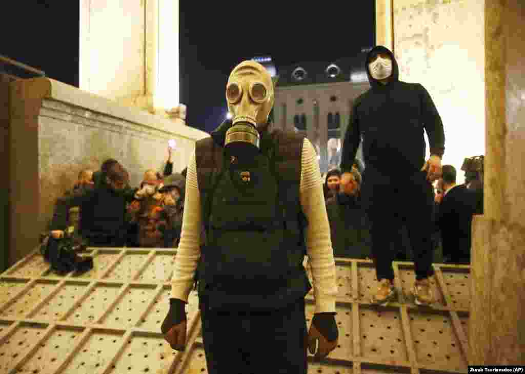 Un protestatar poartă o mască de gaze la intrarea în clădirea parlamentului, pe bulevardul Shota Rustaveli din Tbilisi, după ce o barieră de oțel, montată pentru a-i opri pe protestatari, a fost răsturnată