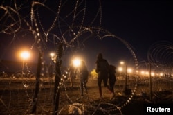 Мигранты ночью нелегально переходят в США из Мексики, преодолевая изгородь из колючей проволоки. Техас, май 2023 года