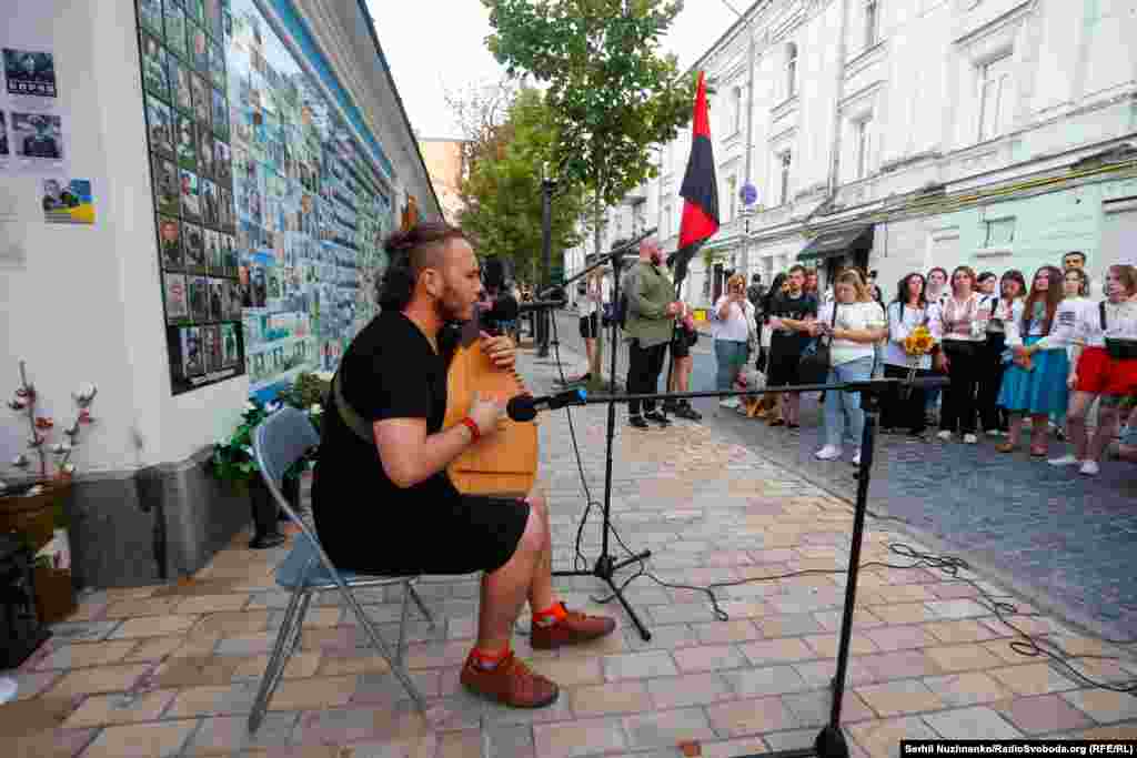 A Ukrainian musician plays next to a wall dedicated to some of Ukraine&#39;s war dead.