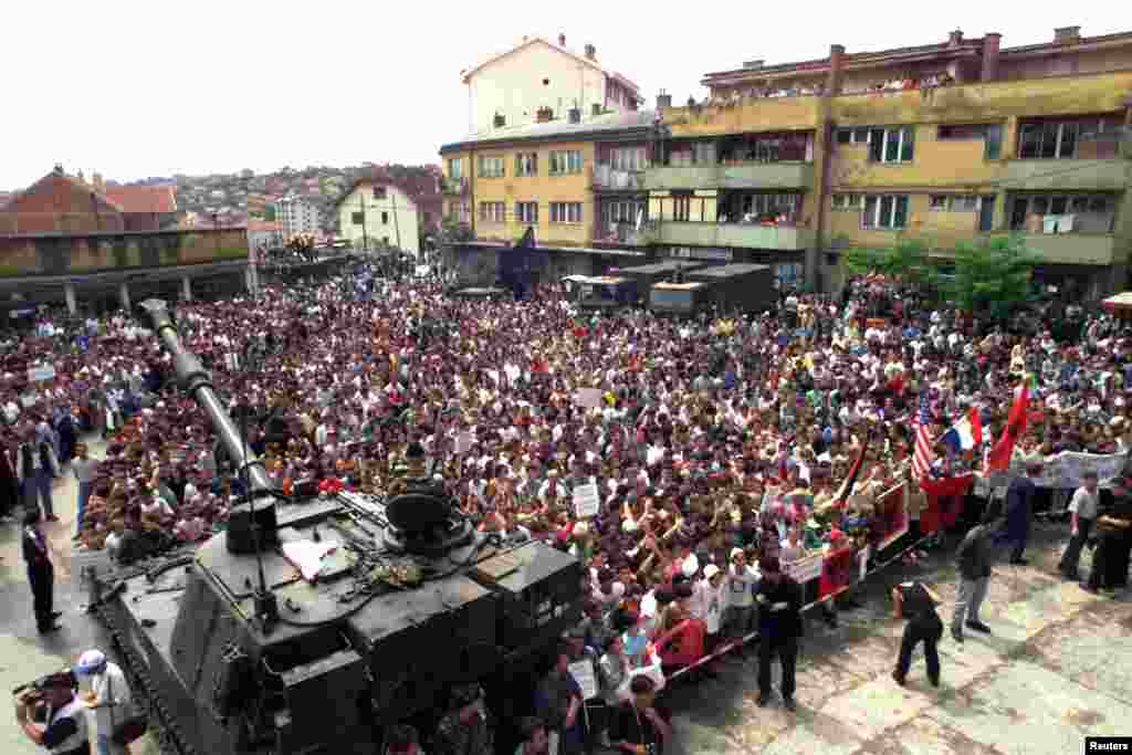 Rahovec 10 korrik 1999:&nbsp; Në këtë fotografi të publikuar nga Reuters, shihen mijëra qytetarë shqiptarë të Rahovecit derisa protestojnë kundër mundësisë që për sigurinë e tyre të kujdesen trupat ruse që kishin hyrë në Kosovë pa një koordinim me NATO-n. &nbsp; 6 qershor 2024: Sheshi në të cilin u zhvillua protesta, sot ka një pamje krejtësisht tjetër. Një xhami e madhe dhe shumë objekte të reja. 