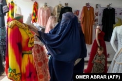 Egy burkába öltözött afgán nő ruhát néz egy üzletben Fajzabadban, Badaksan tartomány fővárosában