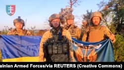 Ukrán katonák állnak a nemzeti zászlóval a Donyecki területen lévő Urozsajne településen 2023. augusztus 16-án