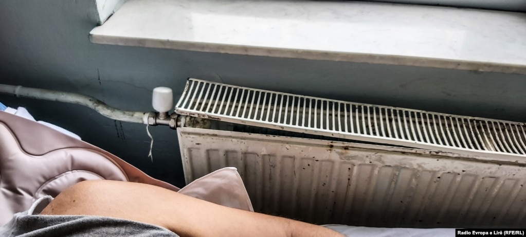 Një pacient i shtrirë në spital, pranë një radiatori gati terësisht të demoluar. 