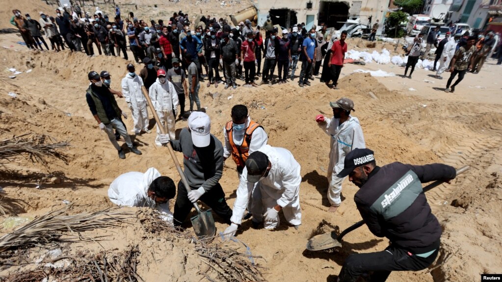 Работници преместват телата на убити палестинци от гроб, разкрит в болницата „Насър“, 21 април 2024 г.