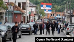 Njerëz duke ecur në një rrugë, sipër së cilës qëndrojnë flamuj të Serbisë, në Zubin Potok, Kosovë, më 31 maj 2023.
