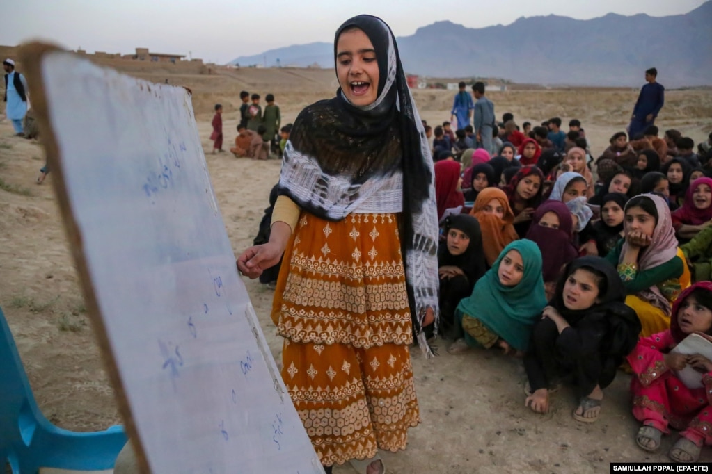 Una ragazza afgana legge una lezione davanti ai suoi coetanei.   Da quando hanno preso il potere nell’agosto 2021 in seguito al ritiro delle truppe internazionali, i talebani afghani hanno imposto al paese un’interpretazione rigorosa della legge islamica della Shari’a che esclude in gran parte le ragazze e le donne dall’istruzione.  La mancanza di istruzione e la riduzione del numero delle insegnanti donne è stata devastante, soprattutto per i bambini che vivono al di fuori delle aree urbane.   